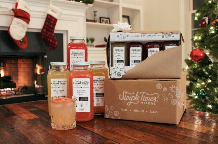 Personalized gift basket of Simple Times Mixers bottles displayed beside a Christmas tree and fireplace