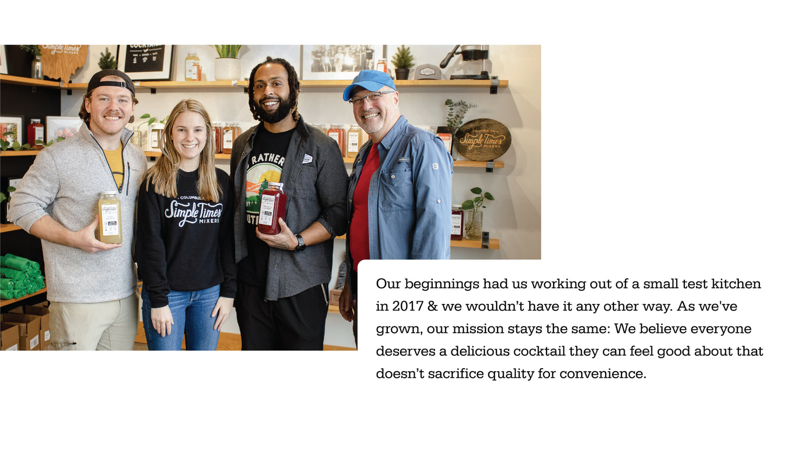 Four Simple Times team members smiling and holding mixer bottles in their shop with shelves of bottled mixers behind them