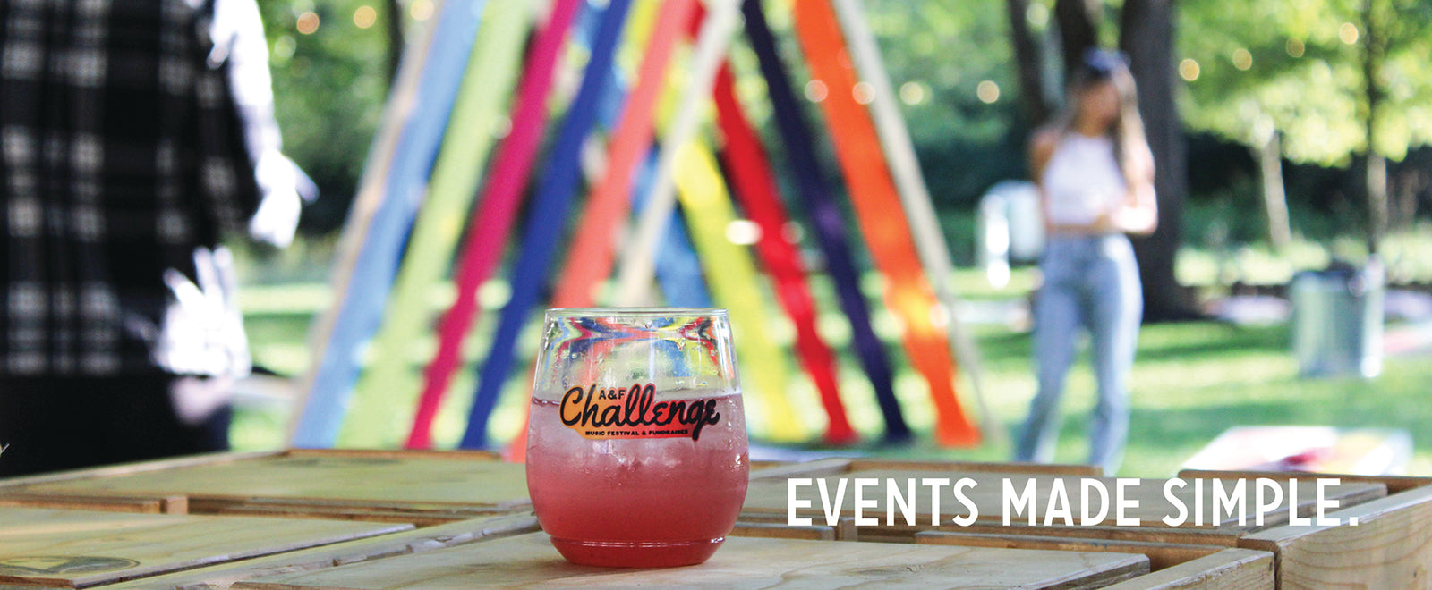 Branded glass of pink mixer on wooden crates at an outdoor festival with colorful ribbons, overlay text EVENTS MADE SIMPLE