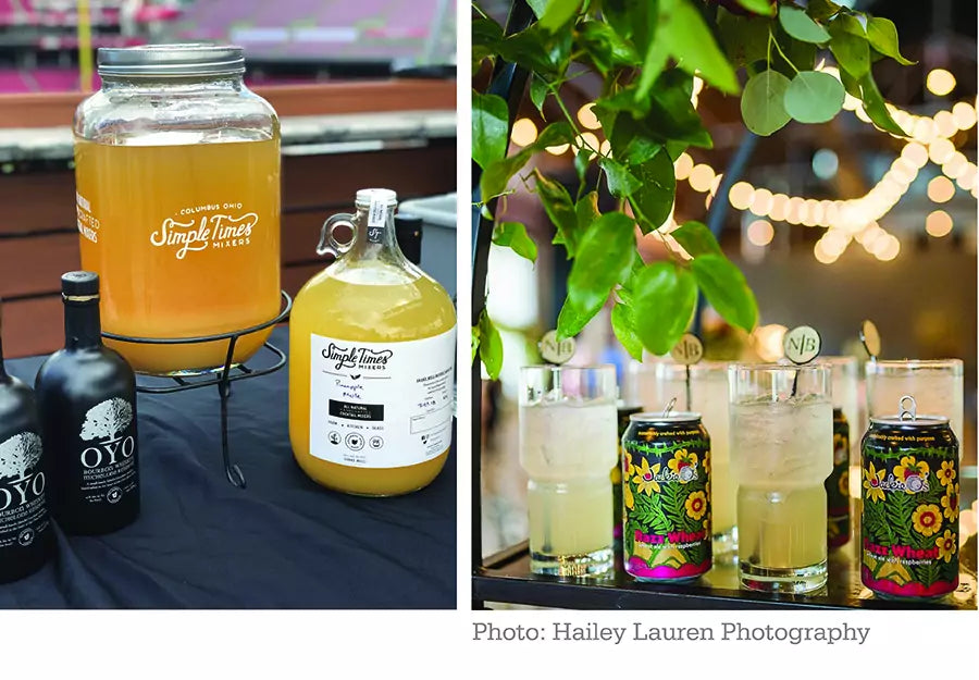 Event cocktail display featuring Simple Times mixer dispenser, jug, glasses, and canned drinks under string lights