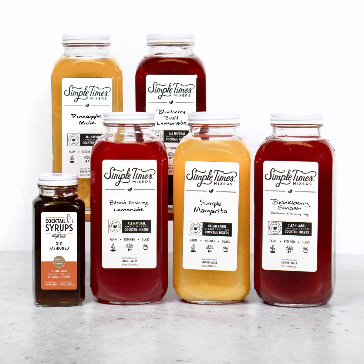 Front view of Build Your Bar Bundle six pack showcasing six flavored mixers and Old Fashioned syrup on a light countertop
