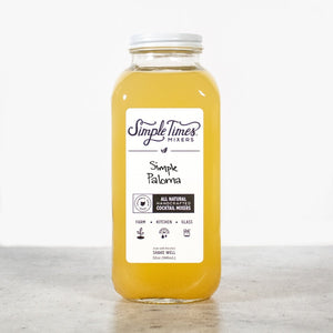 Front view of Simple Paloma cocktail mixer bottle showcasing its yellow grapefruit and lime blend on a light gray surface