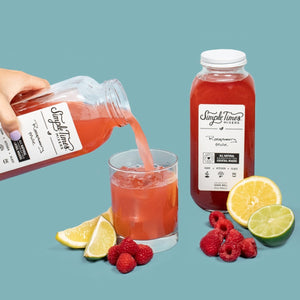 Raspberry Mule cocktail mixer being poured into a glass with raspberries, lemon, and lime