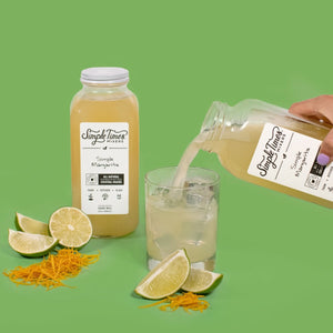 Simple Margarita cocktail mixer poured into a glass with lime wedges and orange zest on a green background