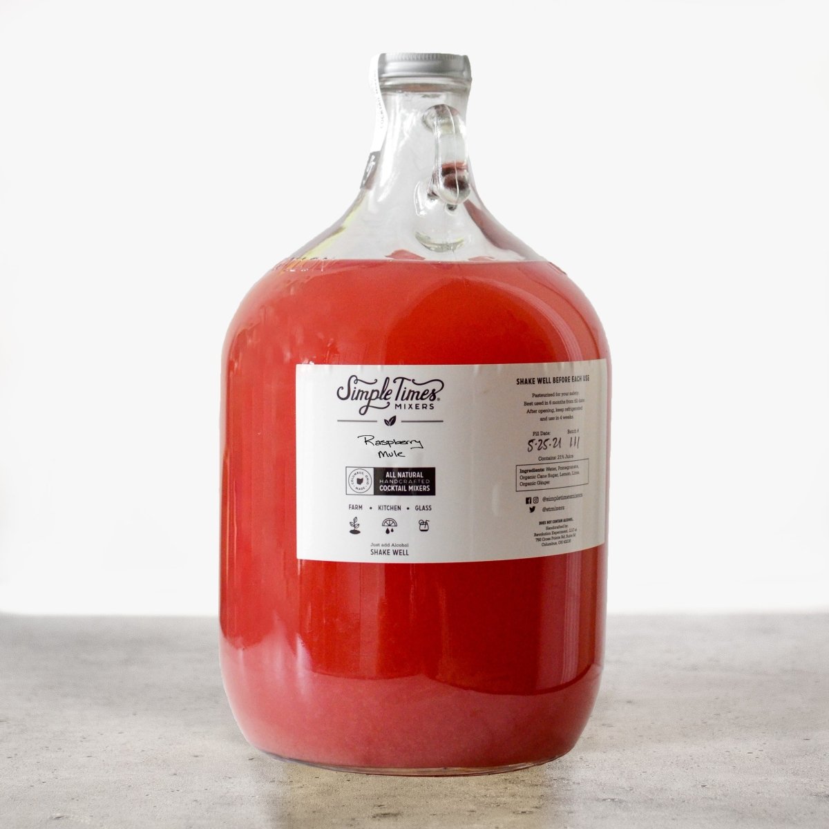 Front view of The Gallon nonalcoholic cocktail mixer in a glass gallon jug with red mixer and white label on a gray surface